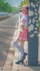 A woman in a pink and white outfit leaning against a pole.