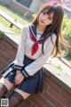 A woman in a school uniform leaning against a brick wall.