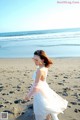 A woman in a white dress walking on the beach.