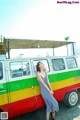 A woman leaning against a colorful van on the beach.