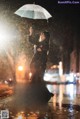 A woman standing in the rain holding an umbrella.