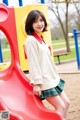 A young woman standing on a red slide in a park.